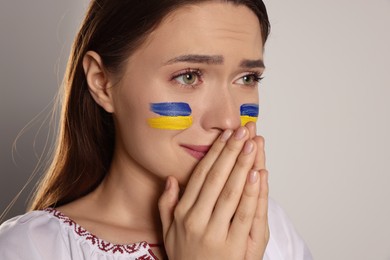 Photo of Sad young Ukrainian woman with clasped hands on beige background, closeup