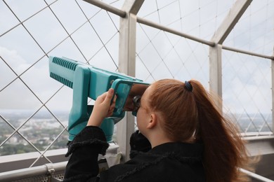Photo of Teenage girl looking through tower viewer at city