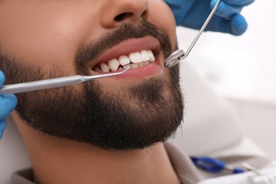 Dentist examining young man's teeth in clinic, closeup
