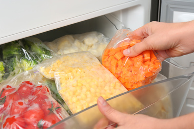 Woman putting plastic bag with carrot in refrigerator with frozen vegetables, closeup