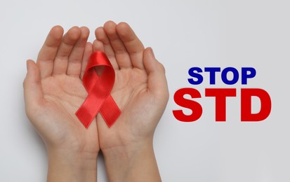 Young woman holding red awareness ribbon on white background, top view. Stop STD 