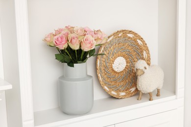 Photo of Shelf with toy sheep, beautiful rose flowers and wicker decor indoors. Interior design
