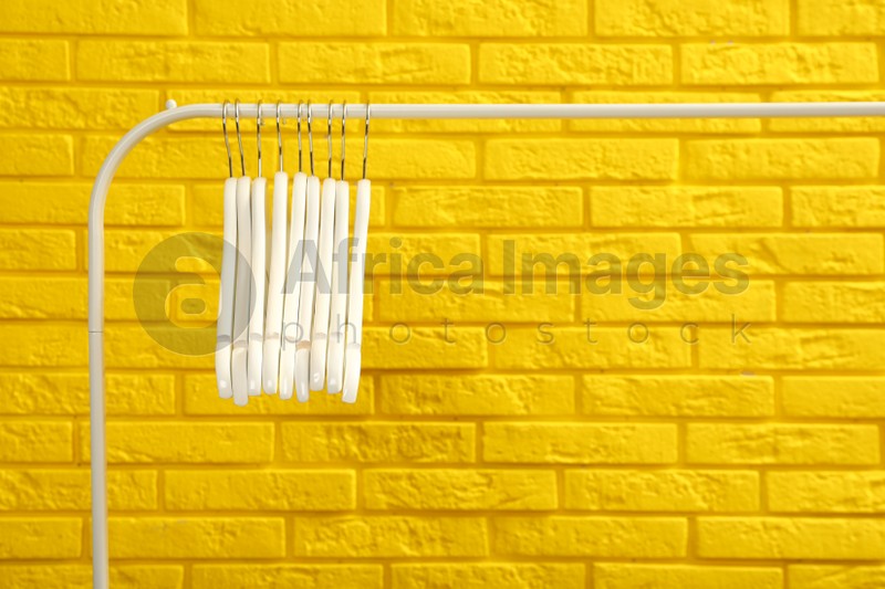 Wardrobe rack with many hangers near yellow brick wall