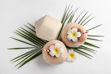 Fresh coconuts with drinking straws and flowers on white background, flat lay