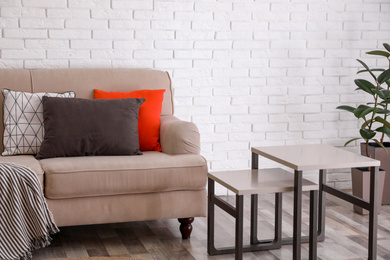 Soft pillows on sofa near white brick wall at home