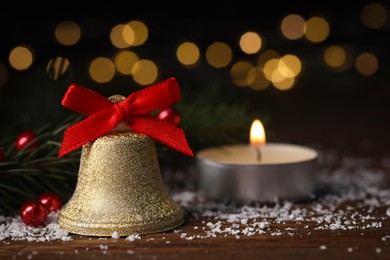 Photo of Bell with red bow and Christmas decor on wooden table against blurred background. Space for text