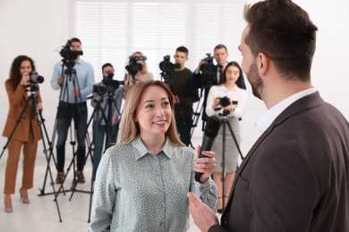 Photo of Professional young journalist interviewing businessman and group of video camera operators on background