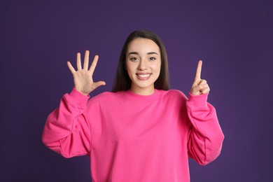 Woman showing number six with her hands on purple background