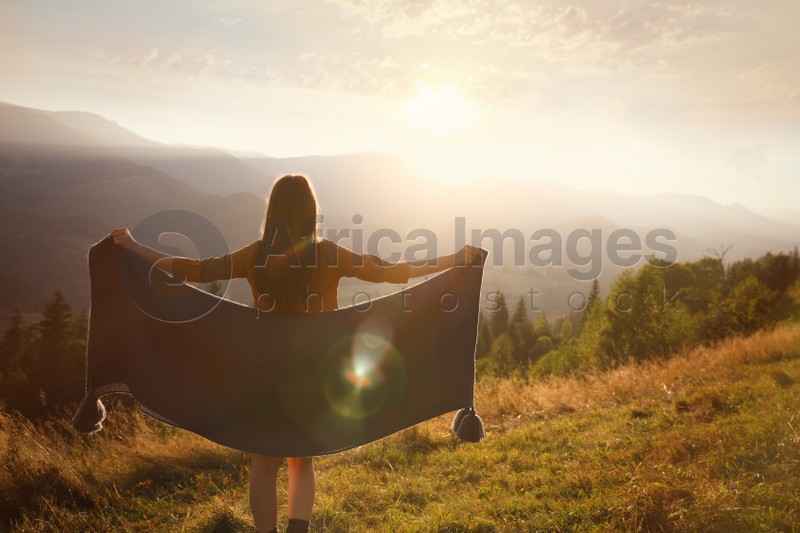 Photo of Woman with cozy plaid enjoying warm sunlight in mountains, back view