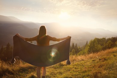 Photo of Woman with cozy plaid enjoying warm sunlight in mountains, back view