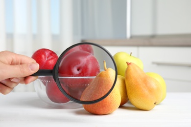 Woman with magnifying glass exploring fruits indoors, closeup. Poison detection
