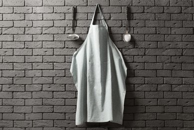 Photo of Clean apron with pattern and kitchen tools on grey brick wall