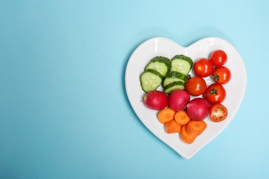 Heart shaped plate with fresh vegetables on color background, top view. Cardiac diet