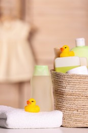 Photo of Wicker basket with baby cosmetic products, bath accessories and rubber ducks on table indoors