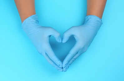 Person in latex gloves showing heart gesture against light blue background, closeup on hands