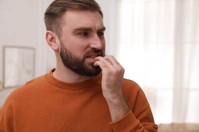 Man biting his nails indoors, space for text. Bad habit
