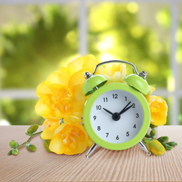 Alarm clock and flowers on table against blurred background. Spring time