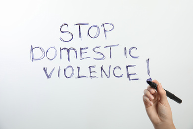 Woman writing phrase STOP DOMESTIC VIOLENCE on glass against white background, closeup