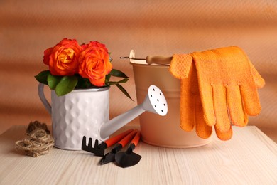 Watering can with beautiful roses, gardening gloves and tools on white wooden table