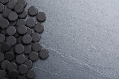 Pile of activated charcoal pills on black table, flat lay with space for text. Potent sorbent