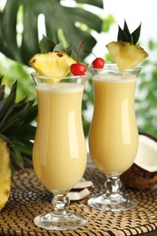 Tasty Pina Colada cocktails and ingredients on wicker mat