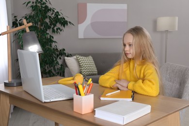 Cute little girl with modern laptop studying online at home. E-learning
