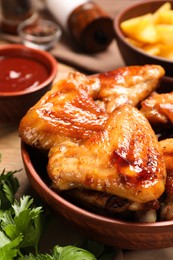 Photo of Bowl with delicious fried chicken wings on wooden table, closeup