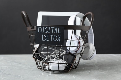 Trash bin with different gadgets and words DIGITAL DETOX on light grey marble table