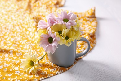 Bouquet of beautiful flowers in cup on orange printed cloth