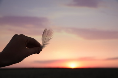 Woman with feather outdoors on sunset, closeup. Healing concept