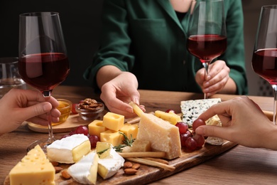 Women with cheese plate and glasses of wine at wooden table, closeup