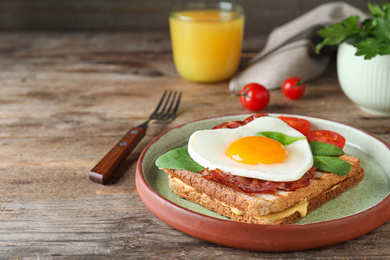 Plate of tasty sandwich with heart shaped fried egg and  bacon on wooden table