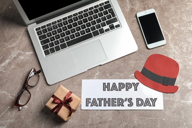 Smartphone, laptop, gift box and card with words HAPPY FATHER'S DAY on grey background, top view