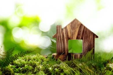 Eco friendly home. House model and coins on green grass outdoors, space for text 