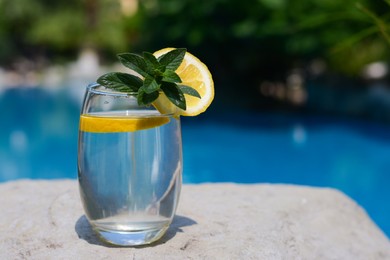 Photo of Refreshing water with lemon and mint on rock outdoors, space for text