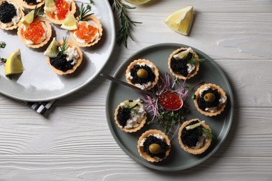 Photo of Delicious tartlets with red and black caviar served on white wooden table, flat lay