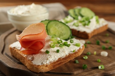 Photo of Delicious sandwiches with cream cheese and other ingredients on wooden board, closeup