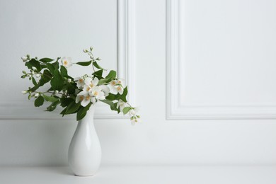 Beautiful bouquet with fresh jasmine flowers in vase on white table indoors, space for text
