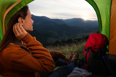 Young woman enjoying mountain landscape in camping tent, view from inside