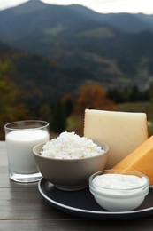 Tasty cottage cheese and other fresh dairy products on grey wooden table in mountains