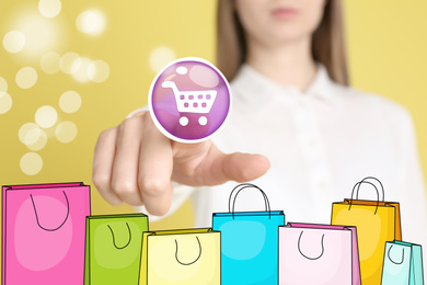 Online shopping. Woman touching button with cart illustration on virtual screen with paper bags, closeup