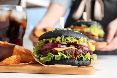 Photo of Board with black burger and french fries served on table in cafe, closeup