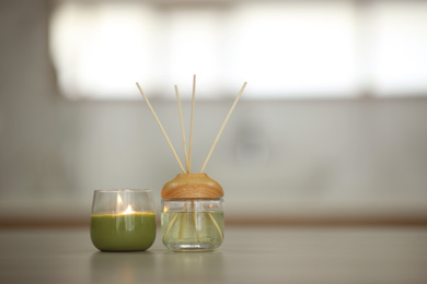 Aromatic reed air freshener and burning candle on table indoors