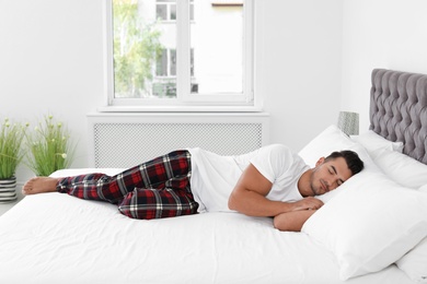 Young man sleeping on bed with soft pillows at home