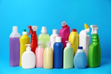 Many bottles of different detergents on light blue background. Cleaning supplies