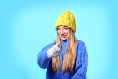 Portrait of emotional young woman in stylish hat, sweater and mittens on color background. Winter atmosphere