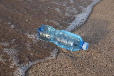 Photo of Plastic bottle of fresh water on wet sand near sea