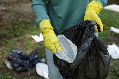 Photo of Woman with plastic bag collecting garbage on green grass outdoors, closeup