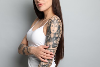 Beautiful woman with tattoos on arms against grey background, closeup