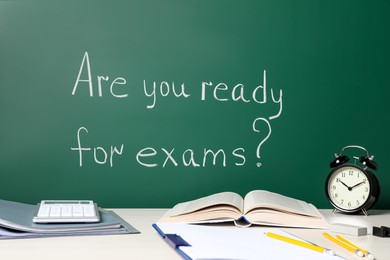 Different stationery and alarm clock on white table near chalkboard with phrase Are You Ready For Exams